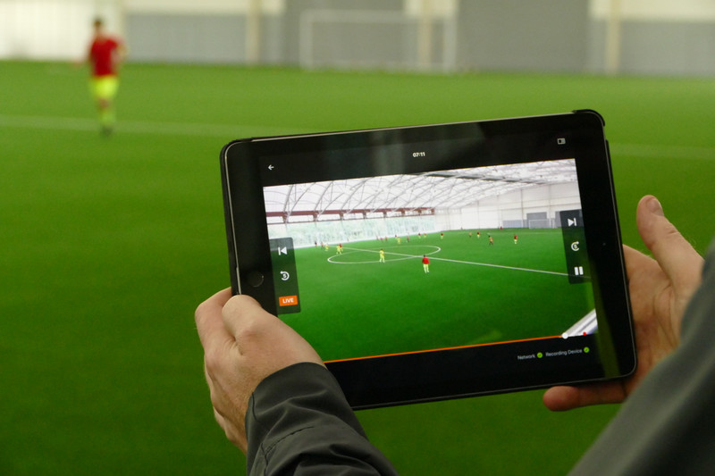 Un hombre vuelve a reproducir el video del partido de fútbol en la tableta desde afuera de la cancha