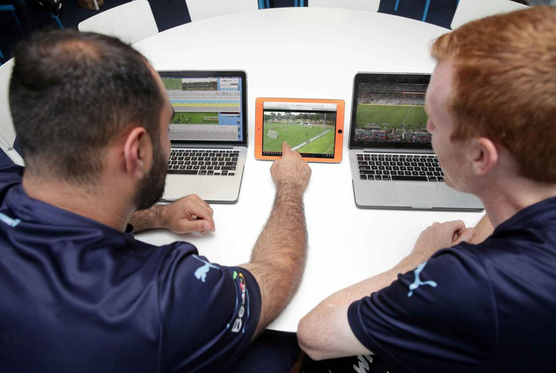 Dos jugadores de fútbol viendo videos del juego en computadoras portátiles y tableta